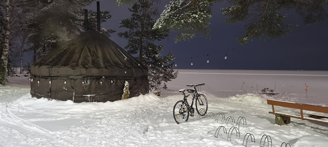 Traditional Finnish sauna beside a snowy lake in a peaceful night setting.