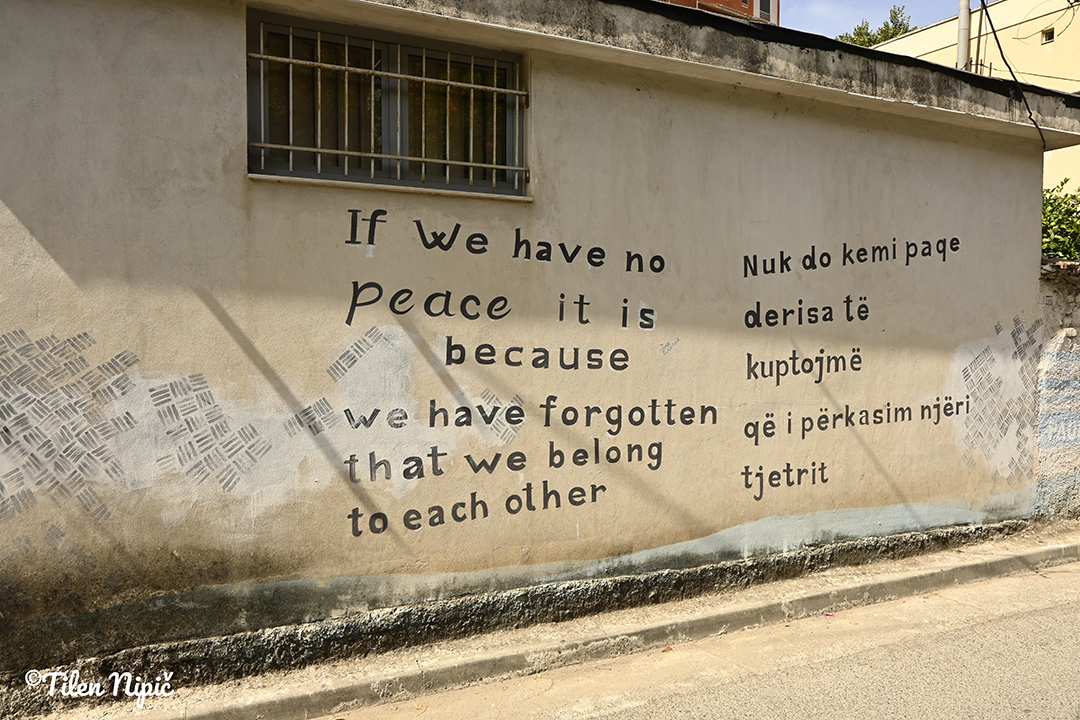 Napis na zidu izraža sporočilo miru in skupnosti v albanskem urbanem prostoru.